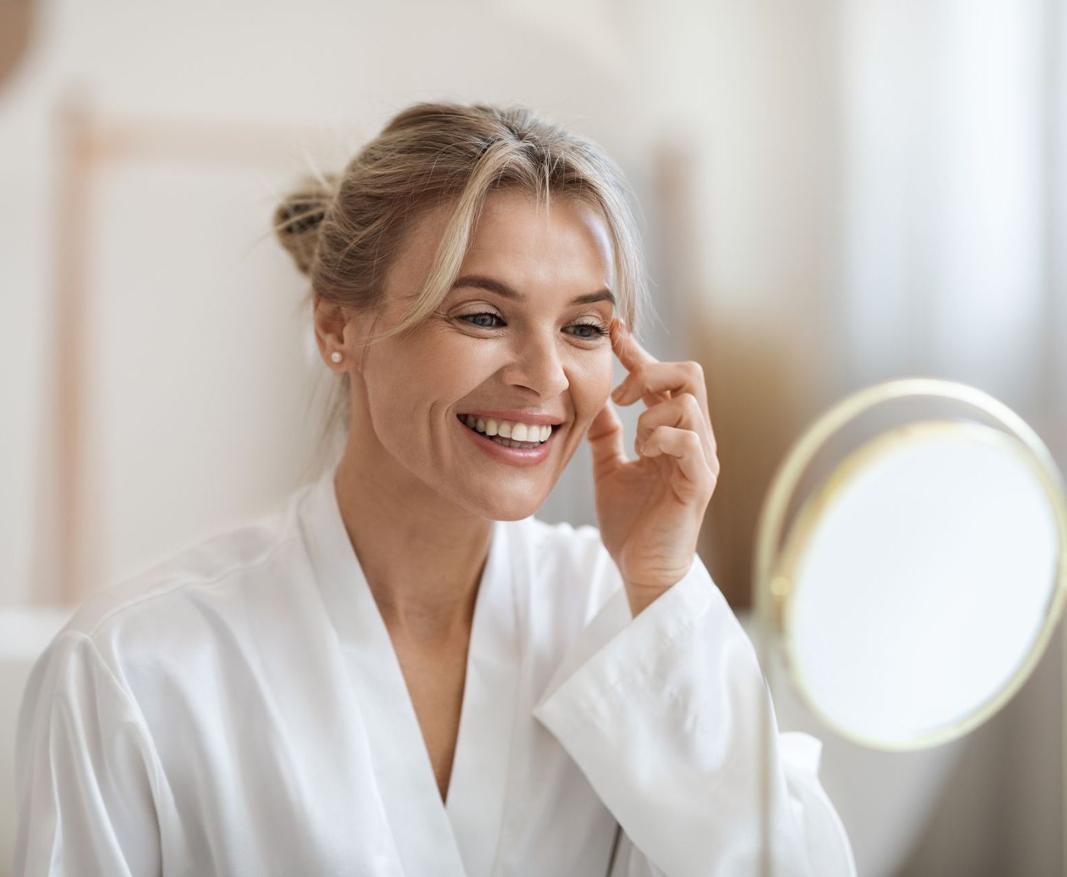 A woman is smiling while looking at her face in a mirror.