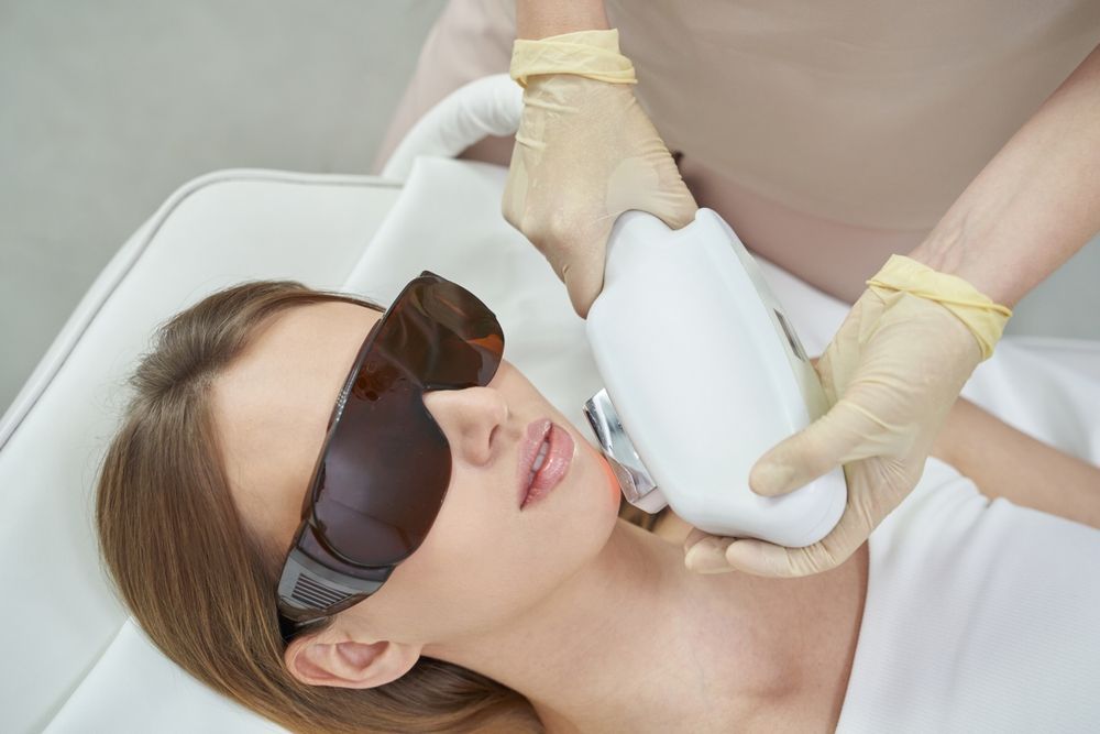 A woman is getting a laser hair removal treatment on her face.