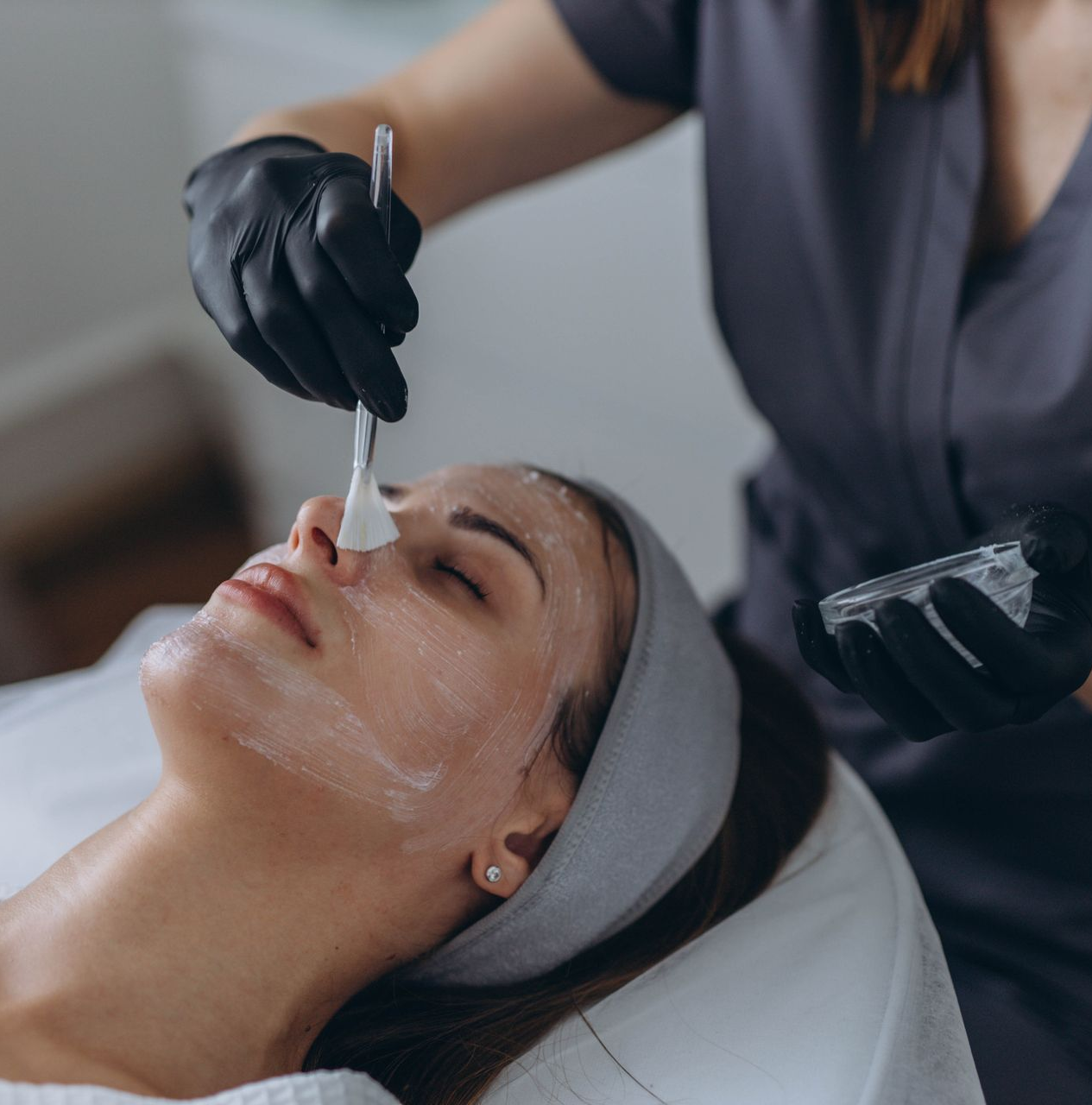 Person receiving facial treatment, esthetician applying product with a brush.