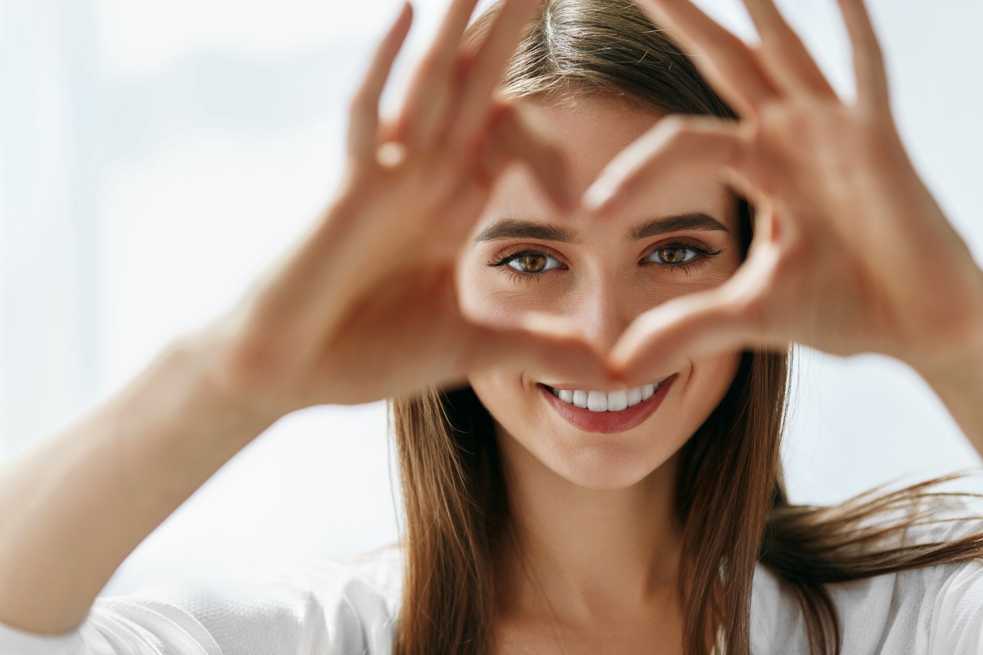 A woman is making a heart shape with her hands over her eyes.