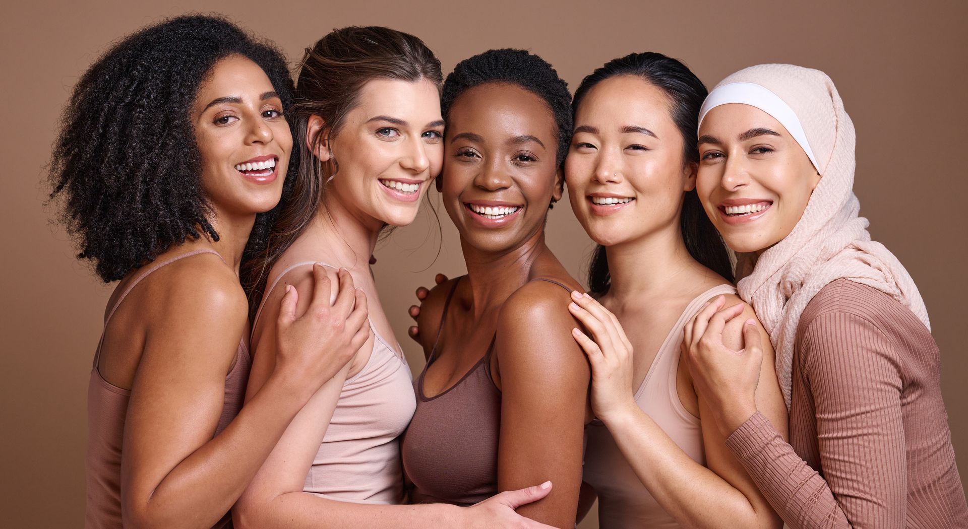 Five smiling women standing close together against a pink background