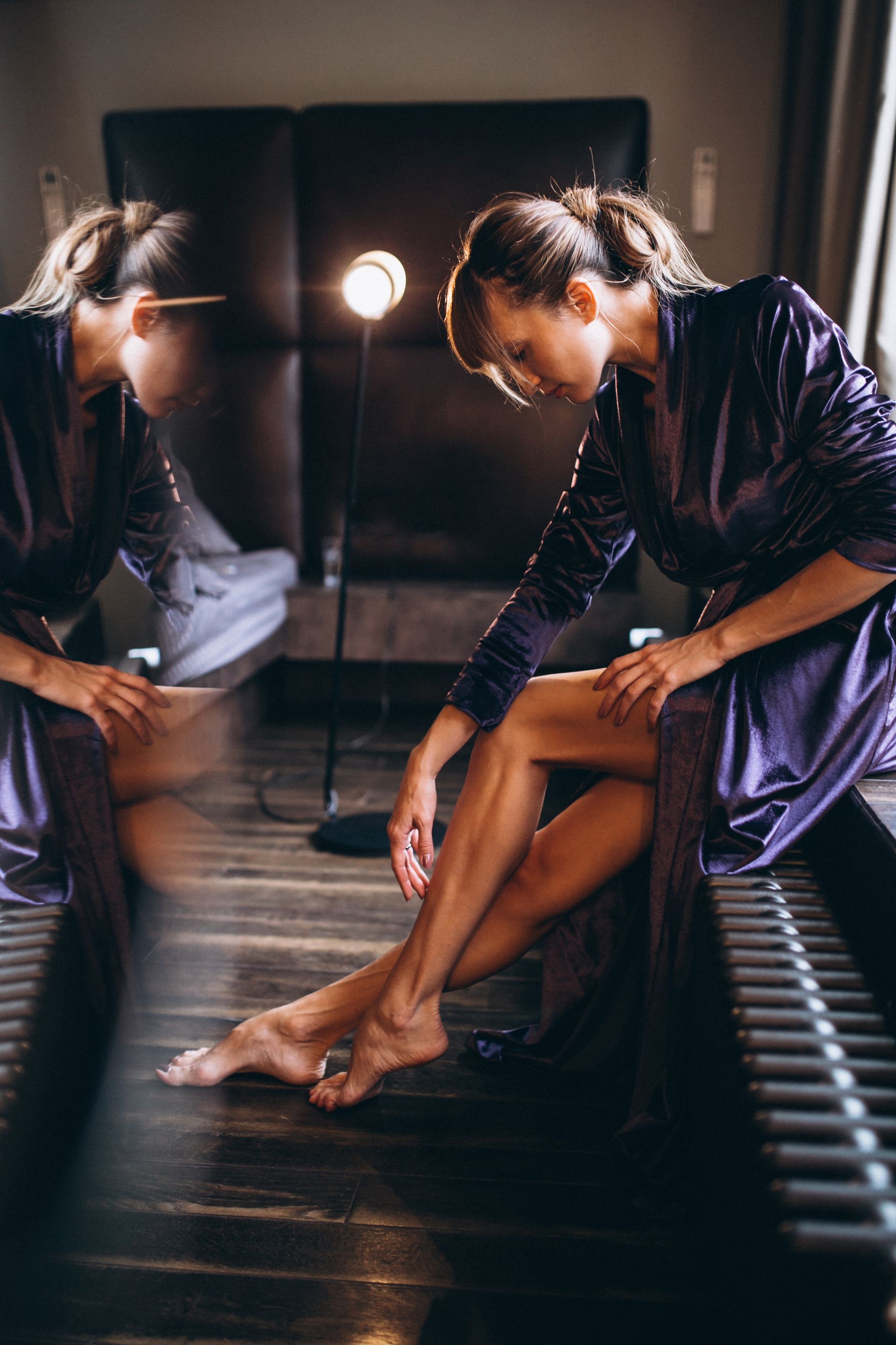 Woman in purple robe sitting, looking at her leg, with mirror reflection.