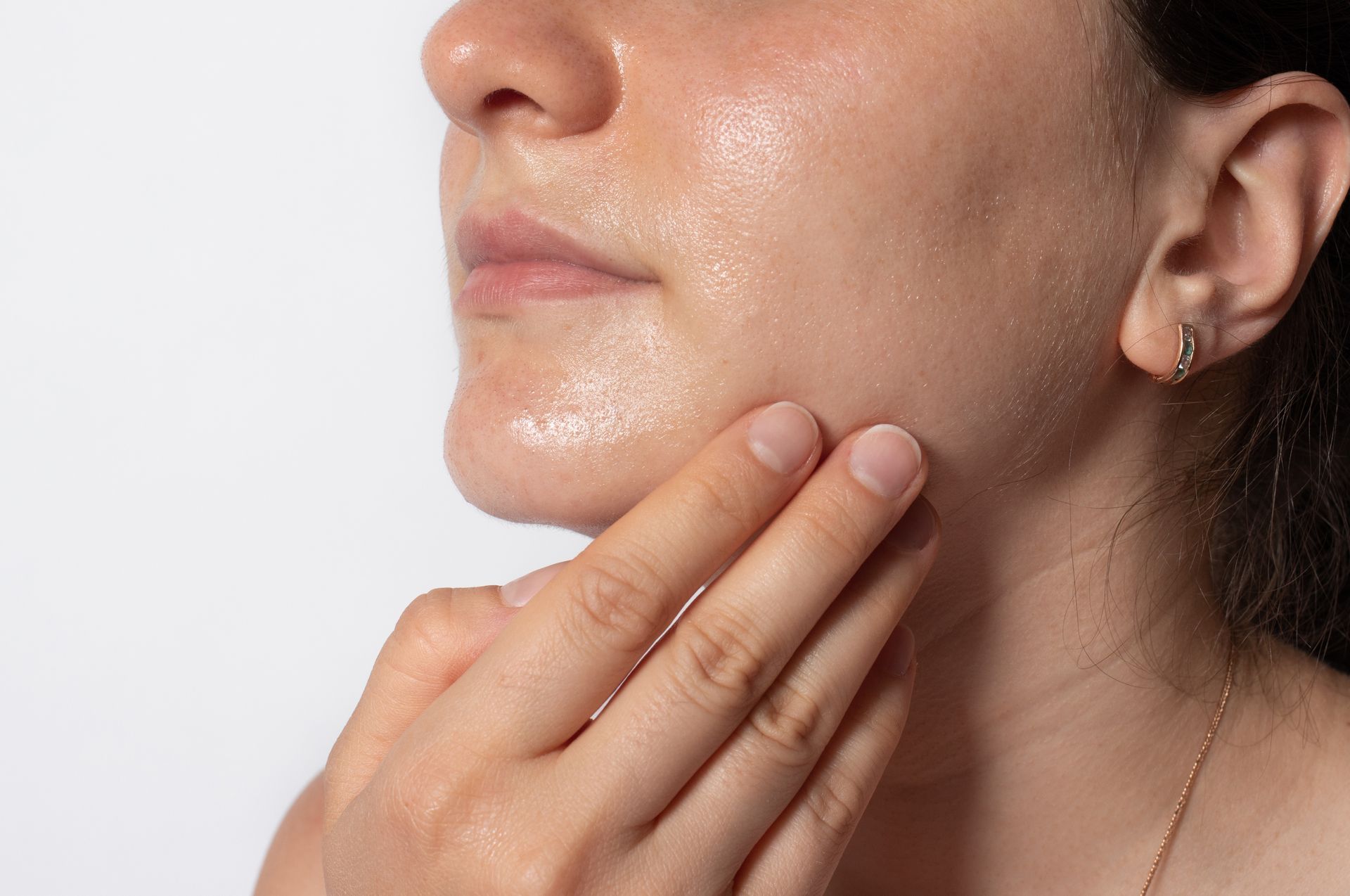 Close-up of a person touching their face, which appears shiny, possibly due to skincare or sweat.