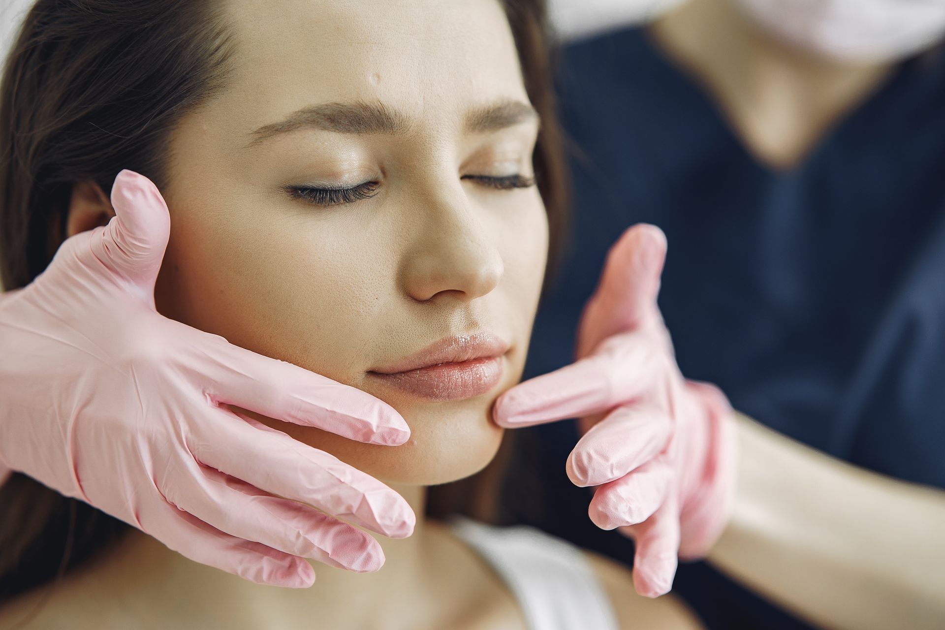 A woman is getting her face examined by a doctor wearing pink gloves.