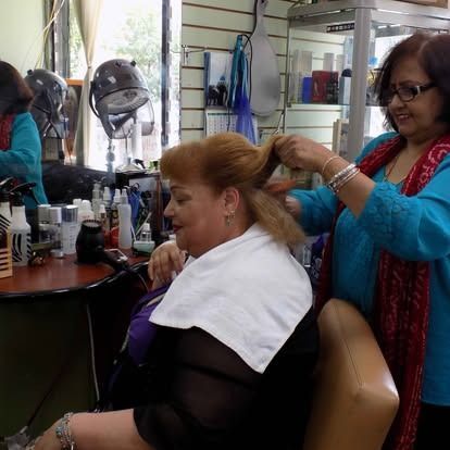A hairdresser styles a customer's hair in a salon. Both women smile.