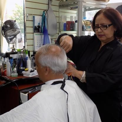 A barber in a black top cuts a man's gray hair in a salon.