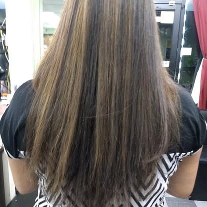 Woman with long, straight brown hair with highlights, wearing a black and white shirt.