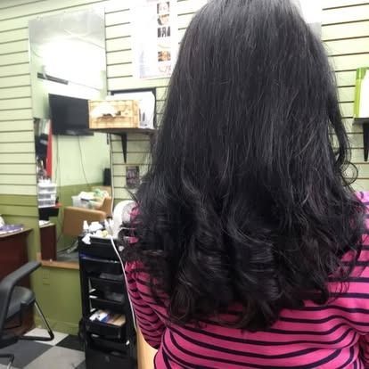 Woman with dark, wavy hair at a salon, wearing a pink striped shirt.
