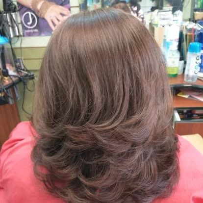 Woman with layered, brown hair in a salon, wearing a red shirt.