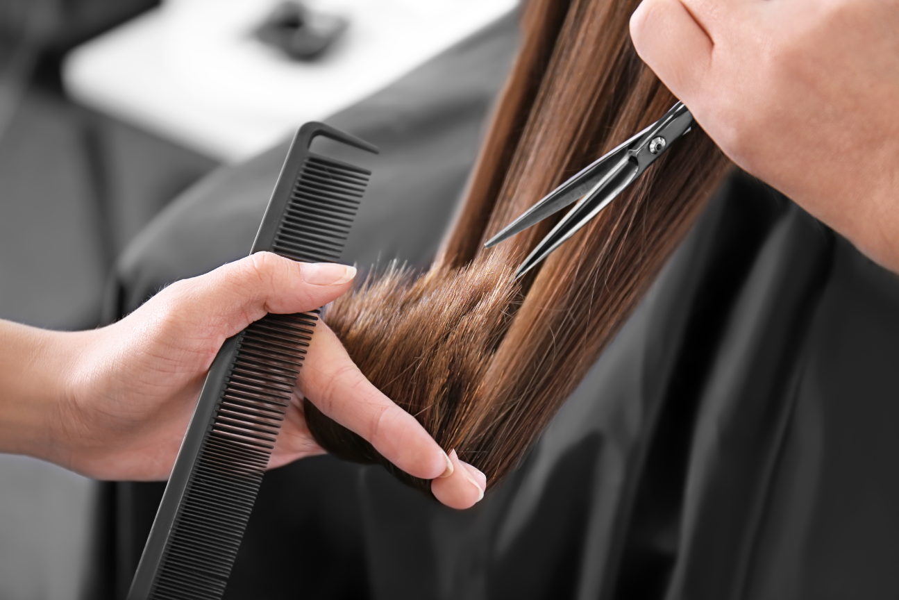 Hairdresser cutting brown hair with scissors and comb in a salon.