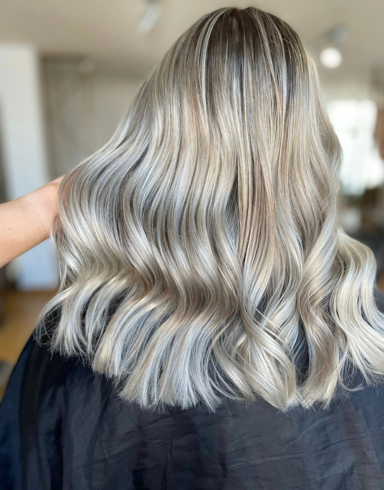 Woman with long, wavy, light blonde hair; hand touches hair.