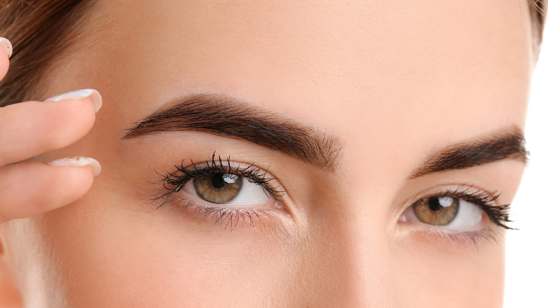 Close-up of woman's face, brown eyebrows, light brown eyes, tan skin, hand near eyebrow.