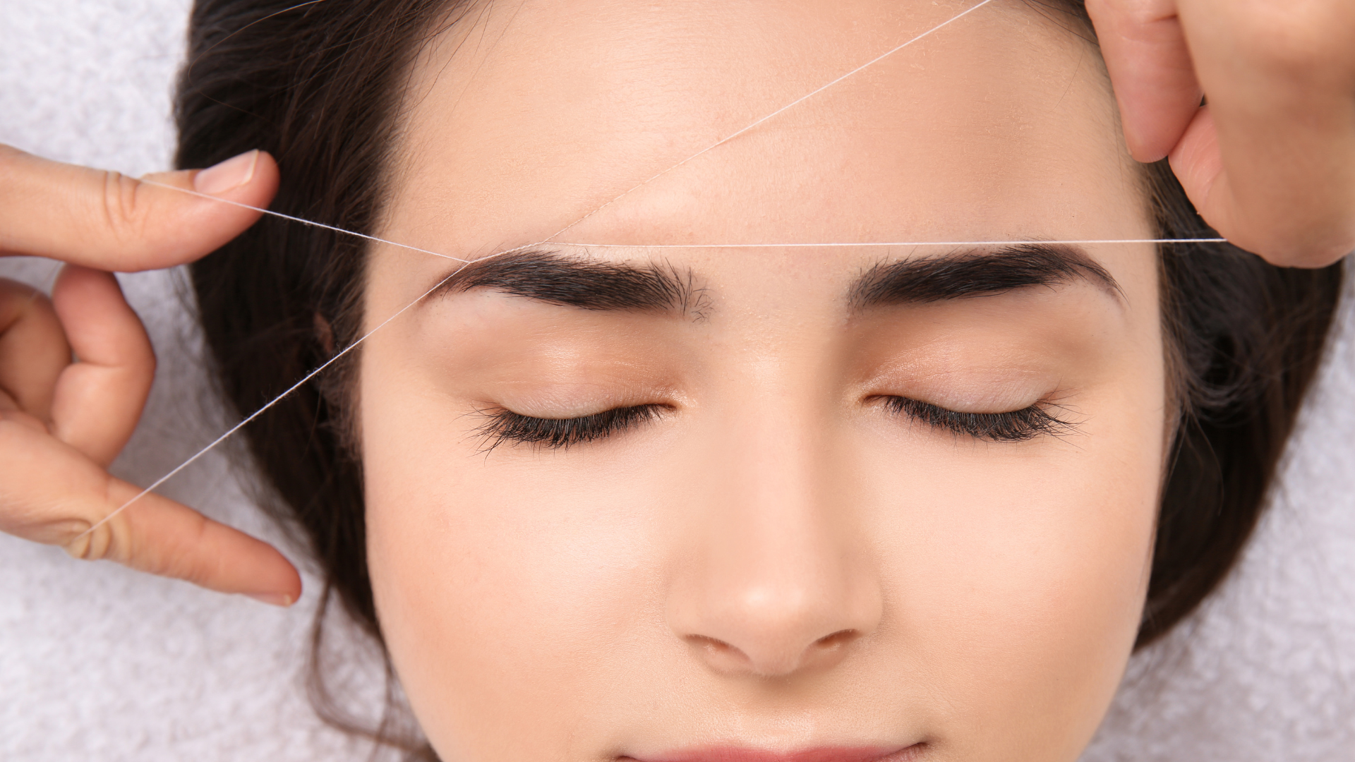 Woman receiving eyebrow threading: thin thread removes unwanted hairs.