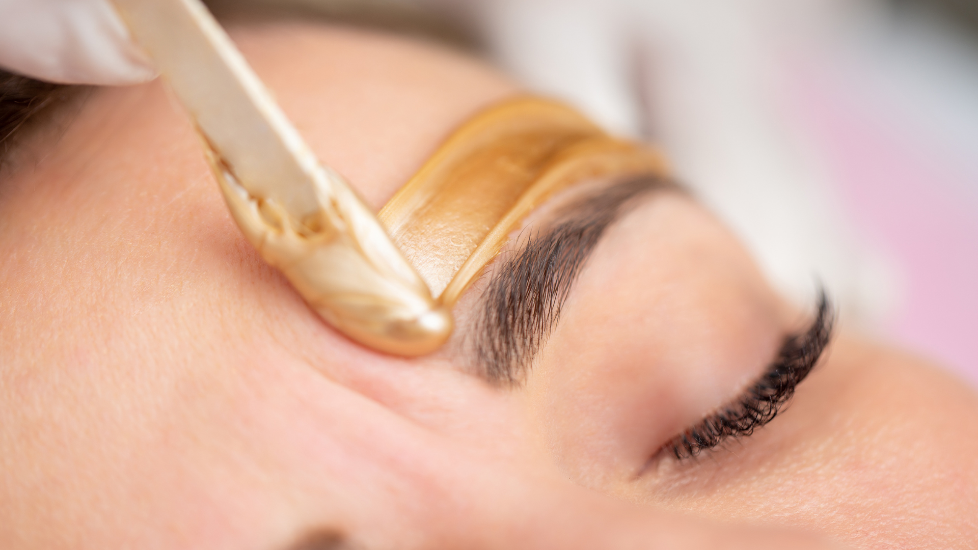 Eyebrow waxing: Technician applies warm wax to shape eyebrow.
