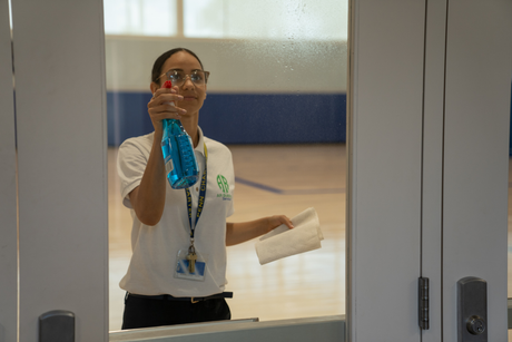 A woman is cleaning a window with a mop in an office.