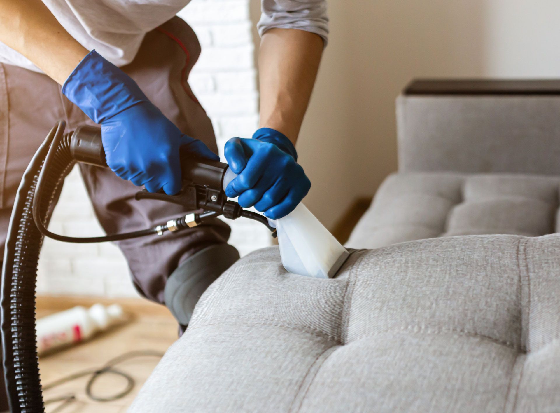 A person is cleaning a couch with a vacuum cleaner.