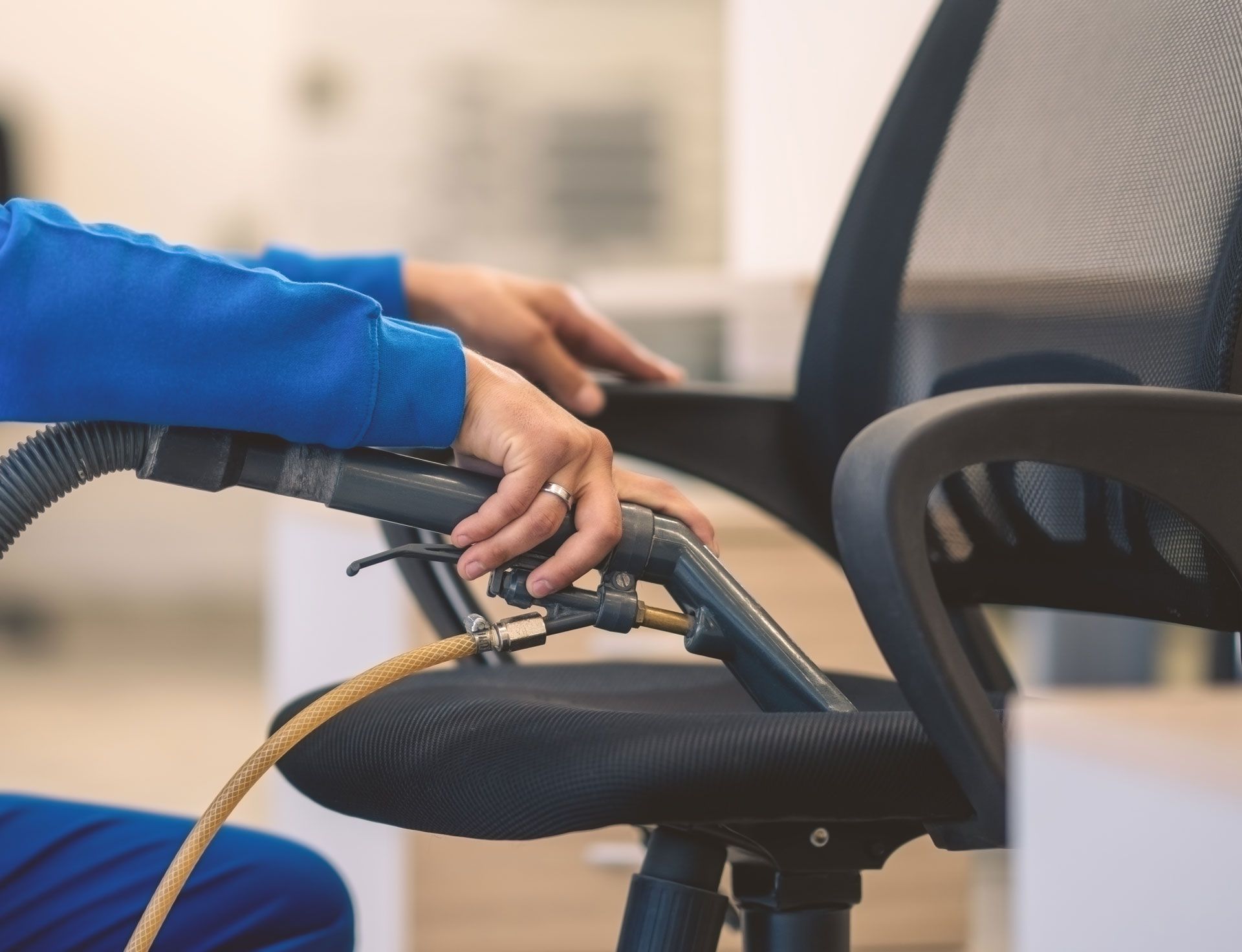 A person is cleaning an office chair with a vacuum cleaner.