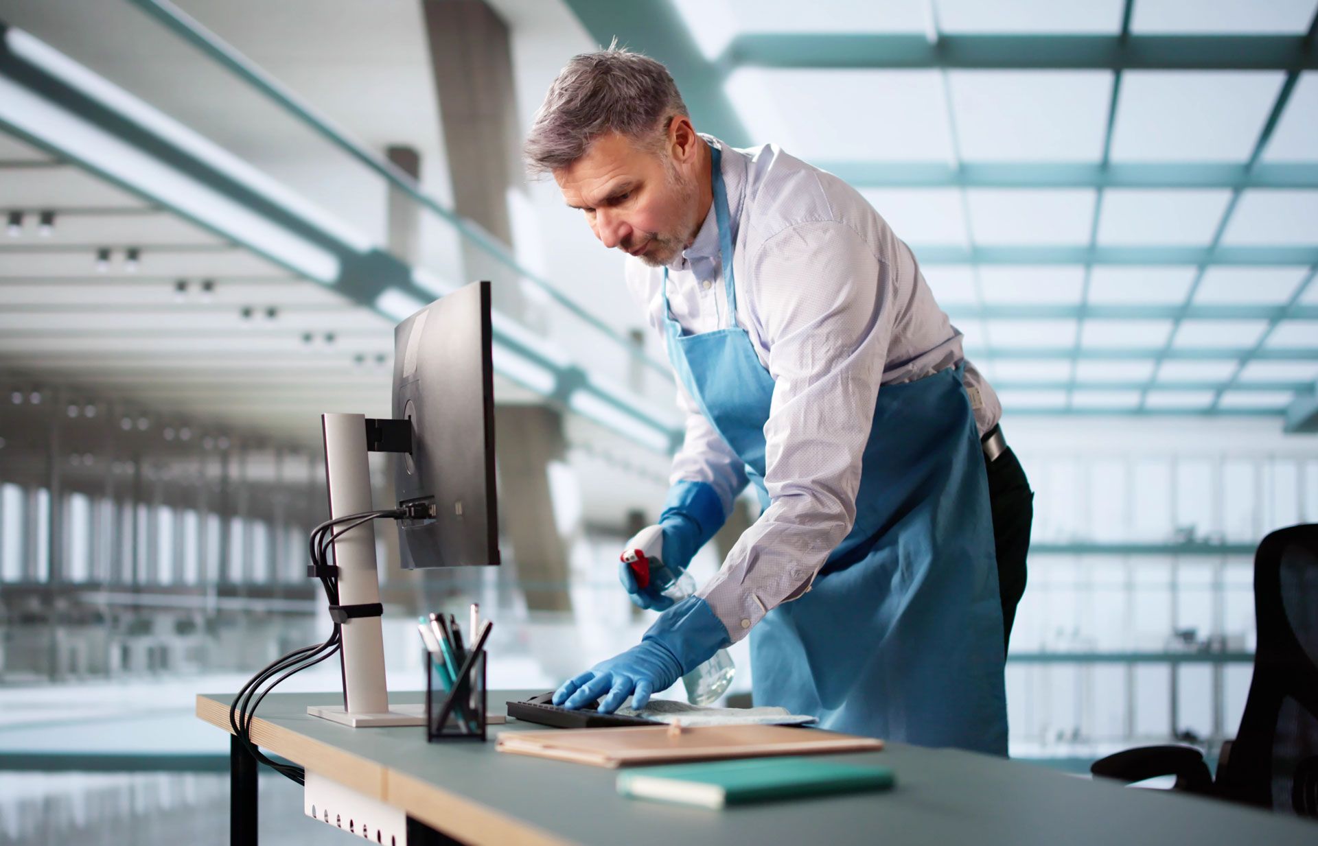 A man is cleaning a desk with a spray bottle in an office.