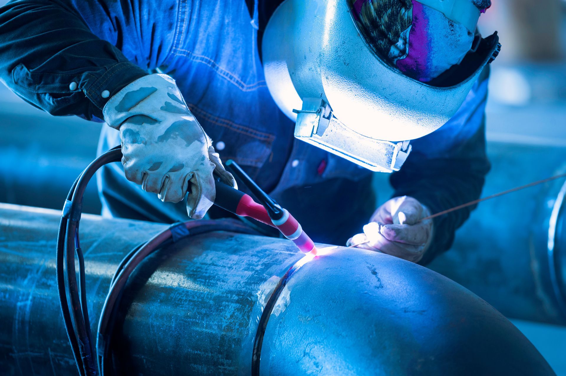 Welder in protective gear fusing a large metal pipe with bright blue sparks