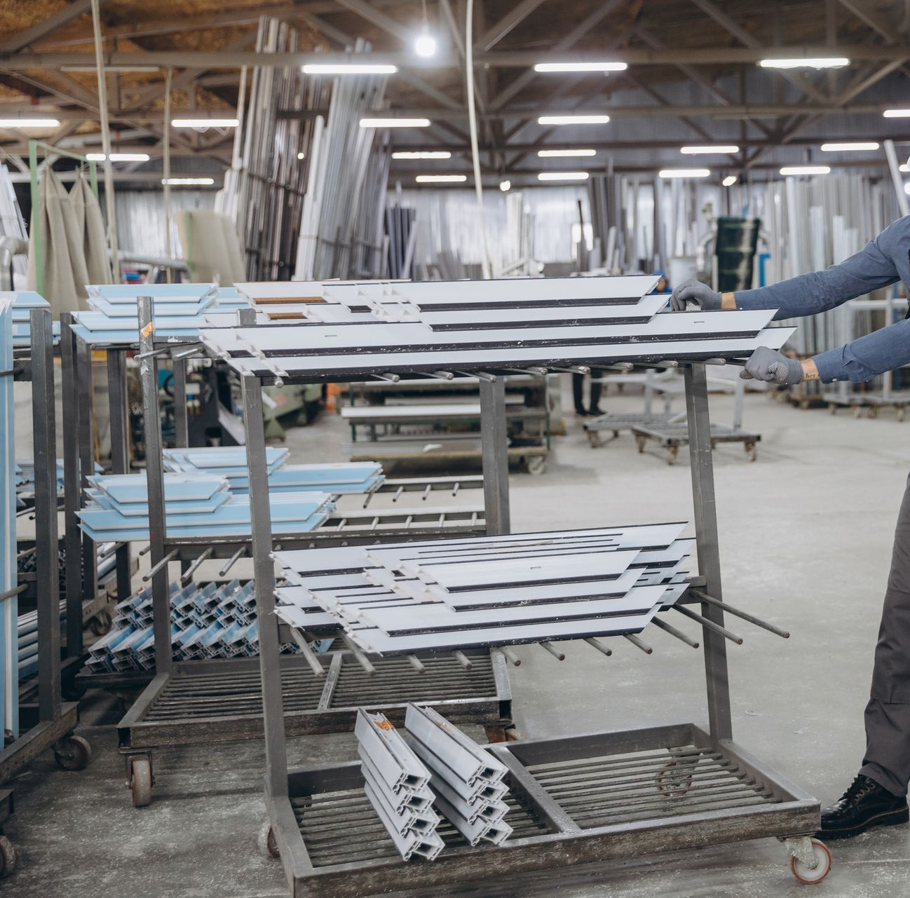 Ouvrier d'usine manipulant des pièces métalliques empilées sur un chariot dans un atelier industriel