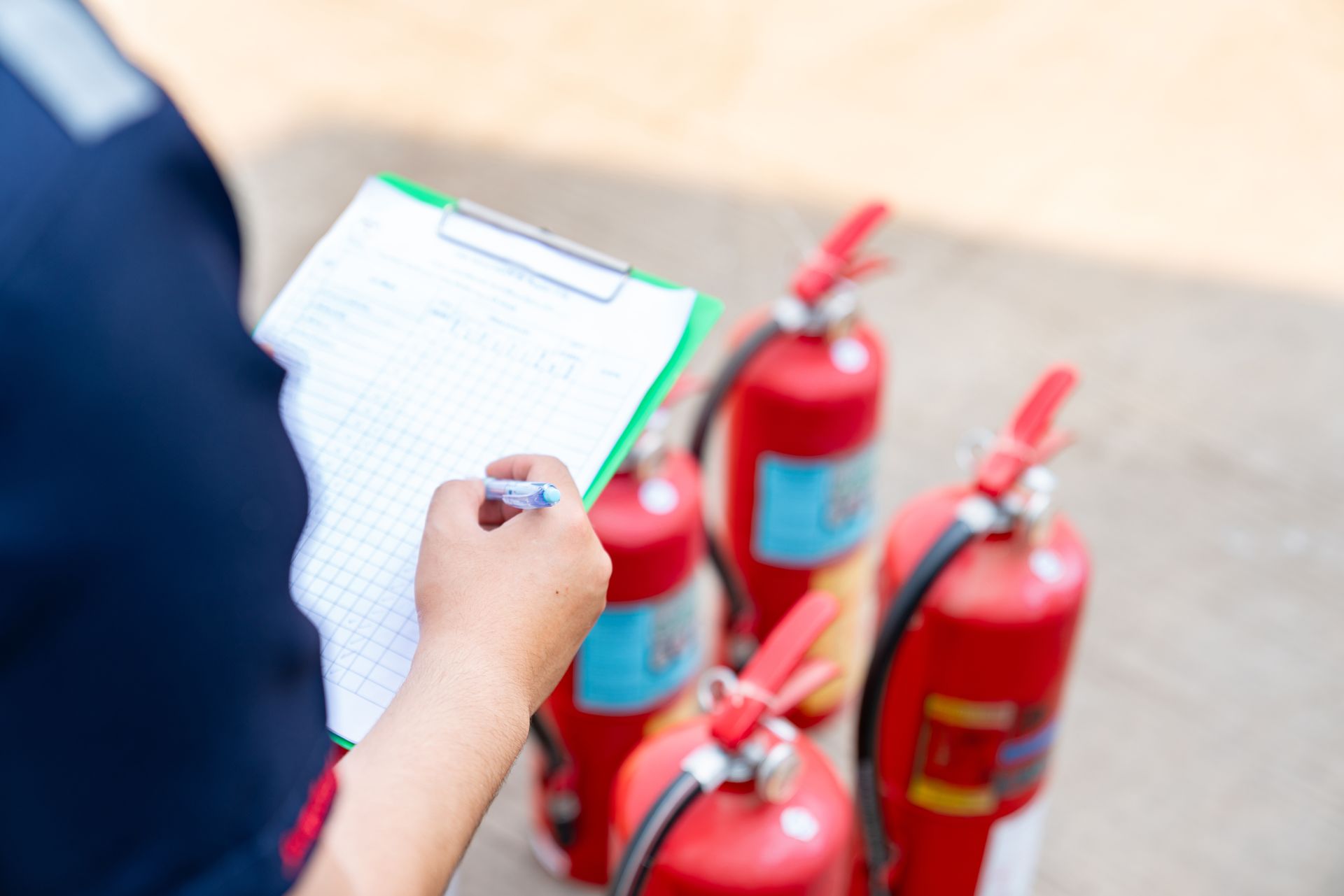 Person checking a clipboard near three red fire extinguishers outdoors