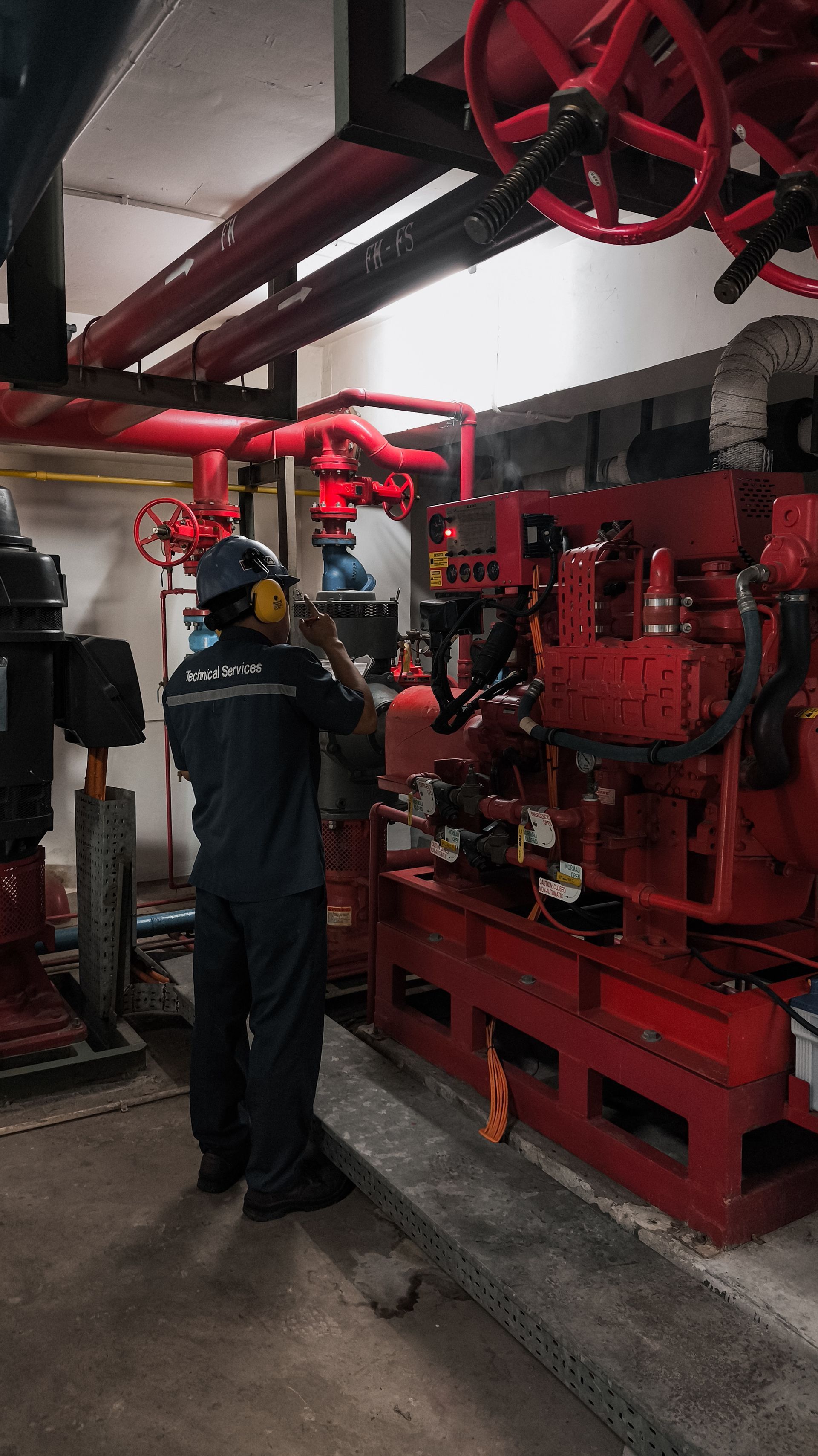 Worker inspecting red industrial machinery in a mechanical room