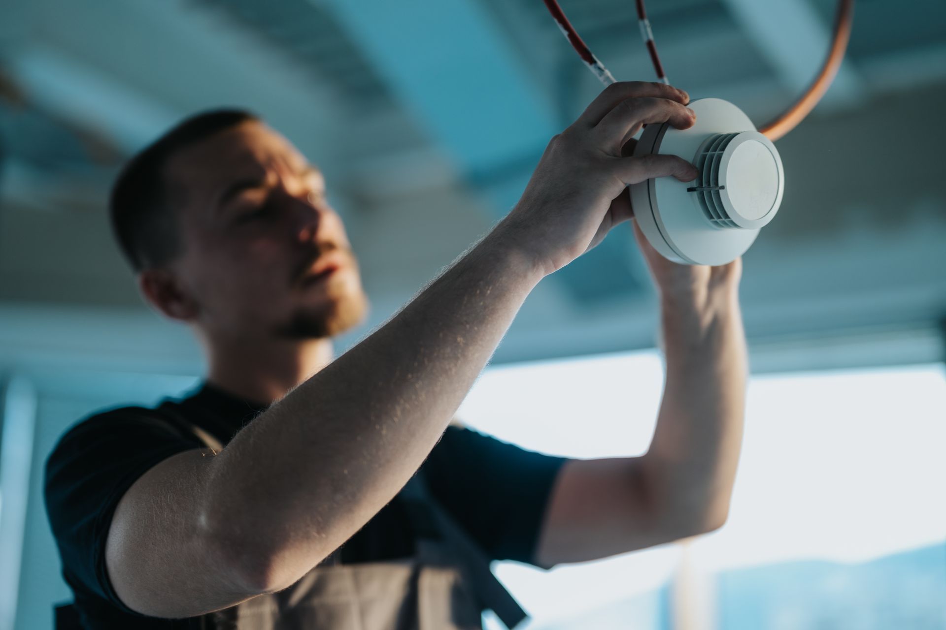 Person installing a white ceiling light fixture with exposed orange wires in a room