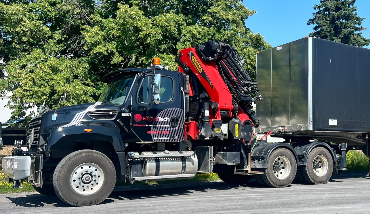 Black tow truck with red crane carrying a large black container on a road