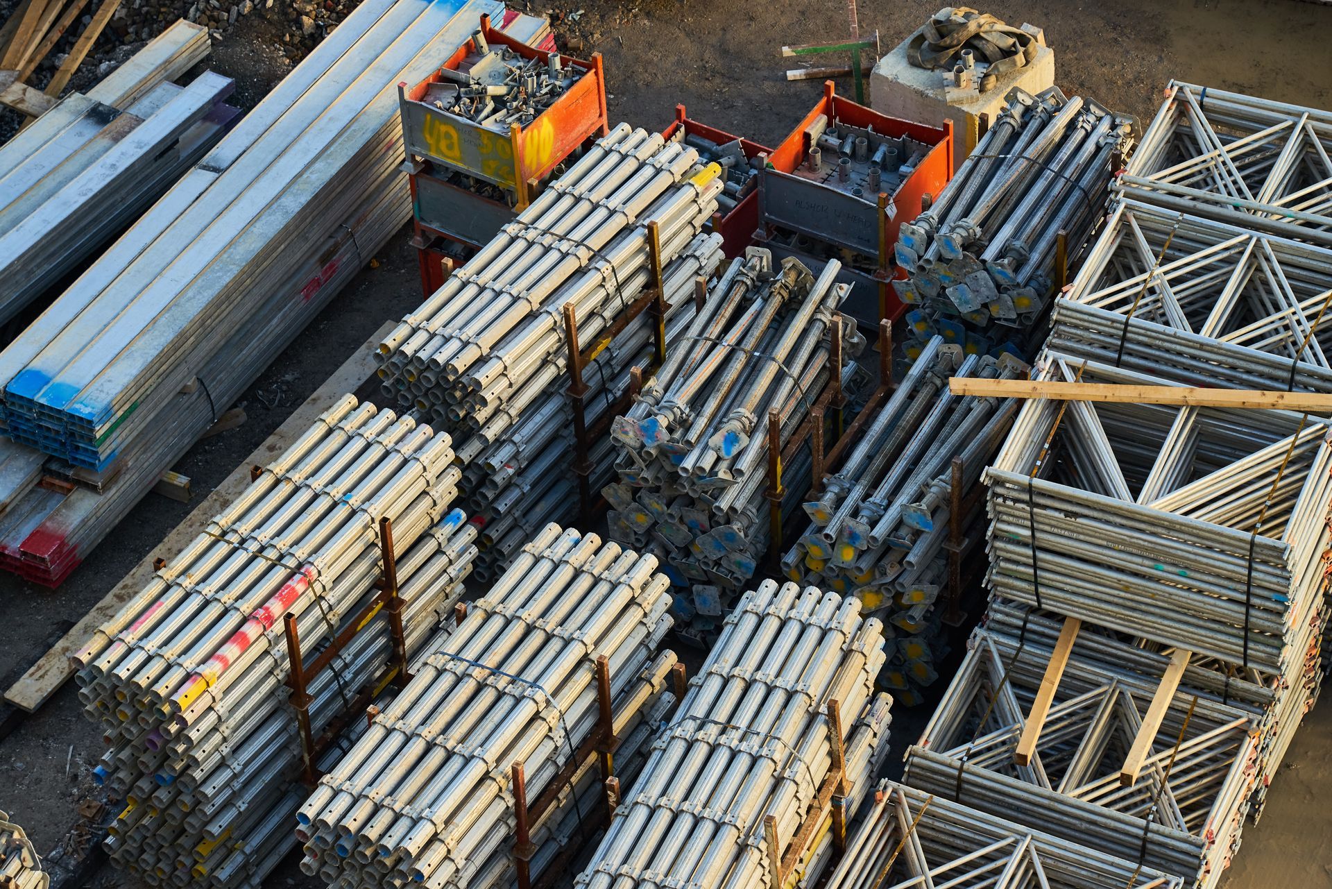 Aerial view of stacked metal beams and pipes in an industrial storage yard with forklifts