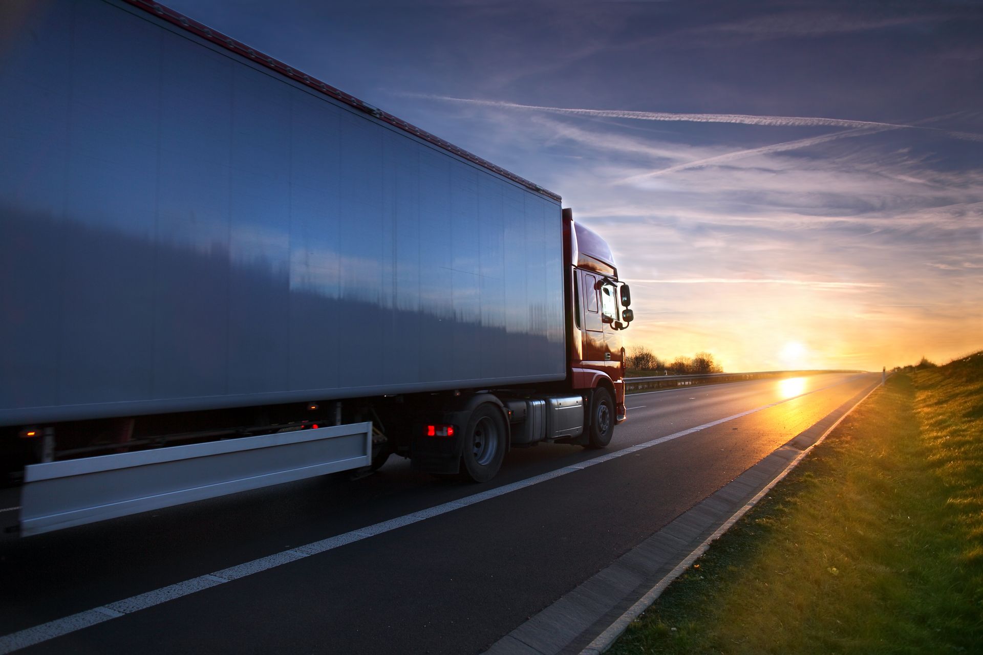 Semi-truck driving on a highway at sunset, with golden light on the horizon
