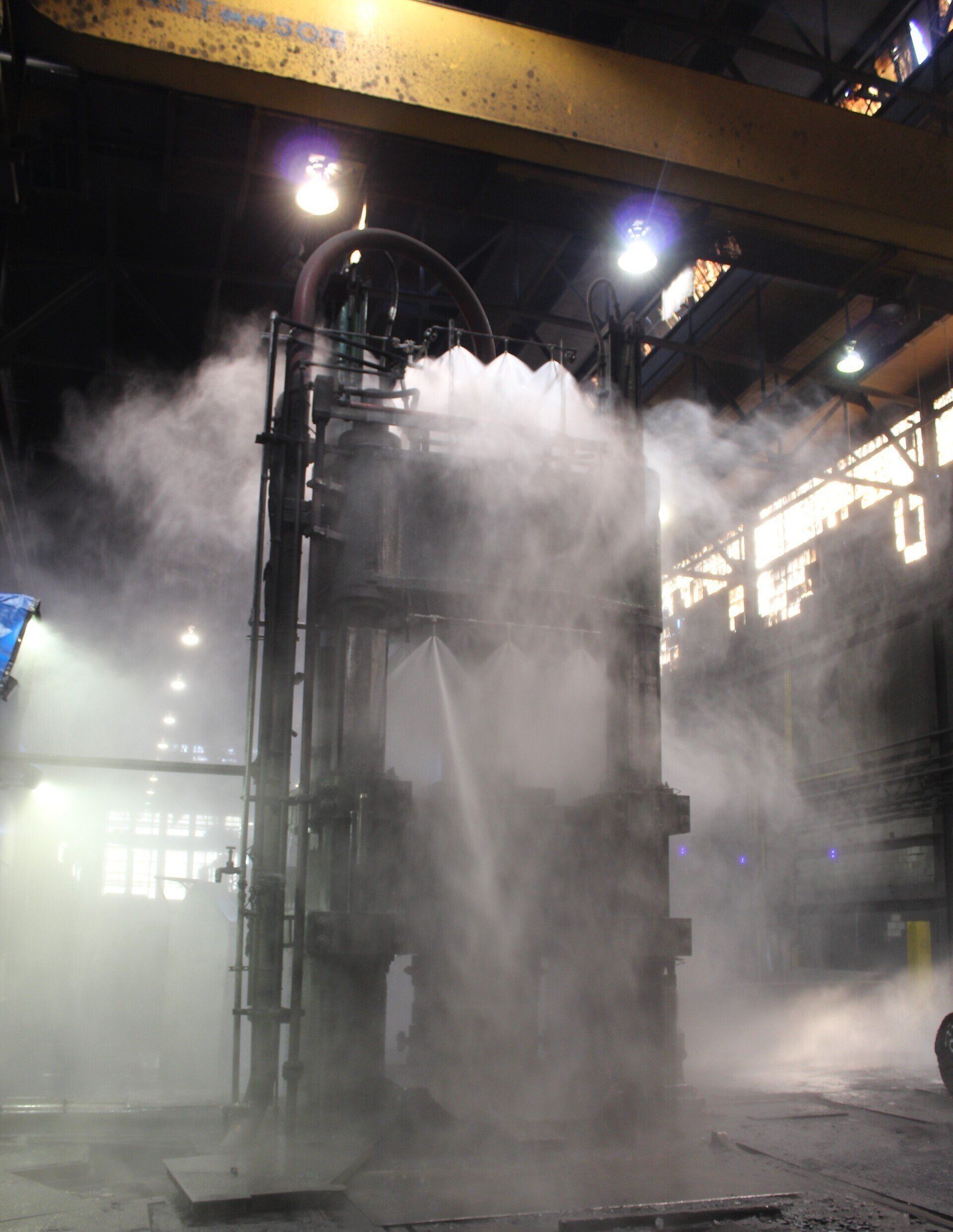 Steam billows around a large industrial machine inside a factory hangar.