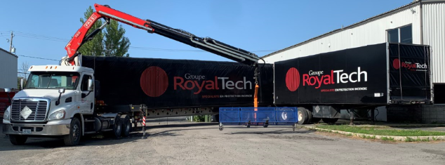 Camion-grue rouge en train de décharger sur un bâtiment de RoyalTech avec signalétique noire.