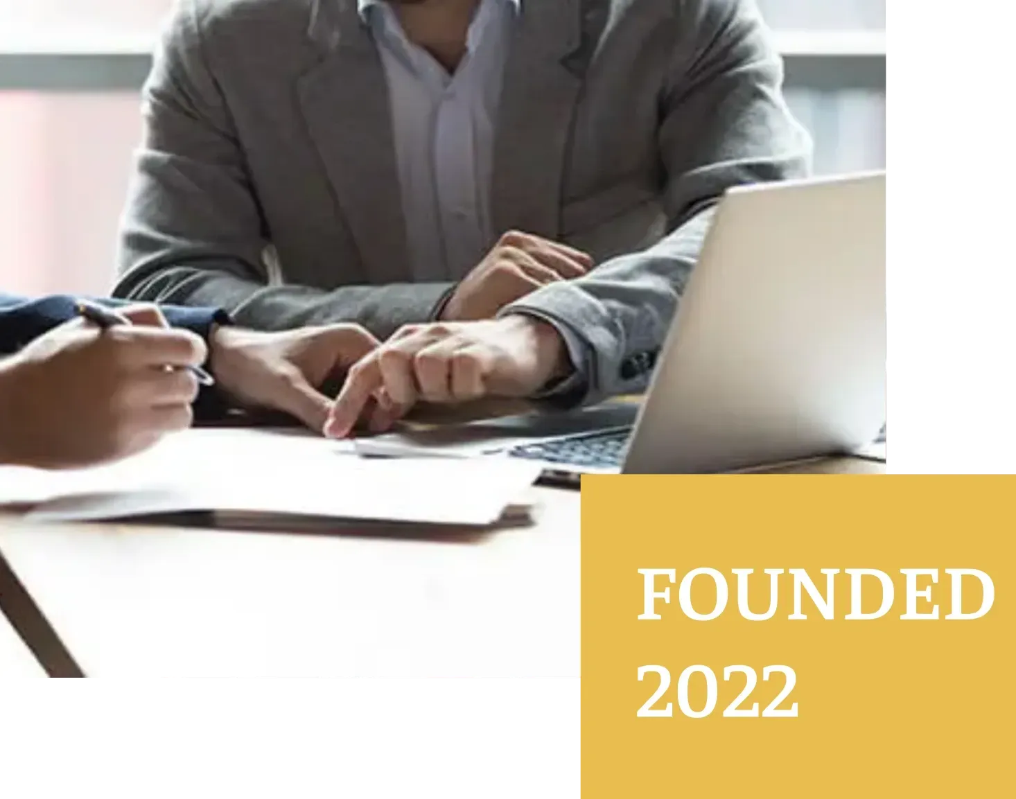 Two people reviewing documents, one pointing, near a laptop; founded 2022.
