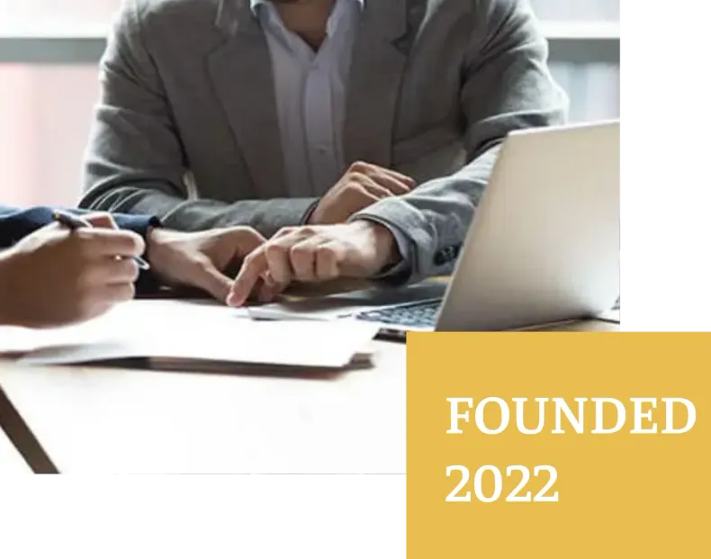 Two people reviewing documents, one pointing, near a laptop; founded 2022.