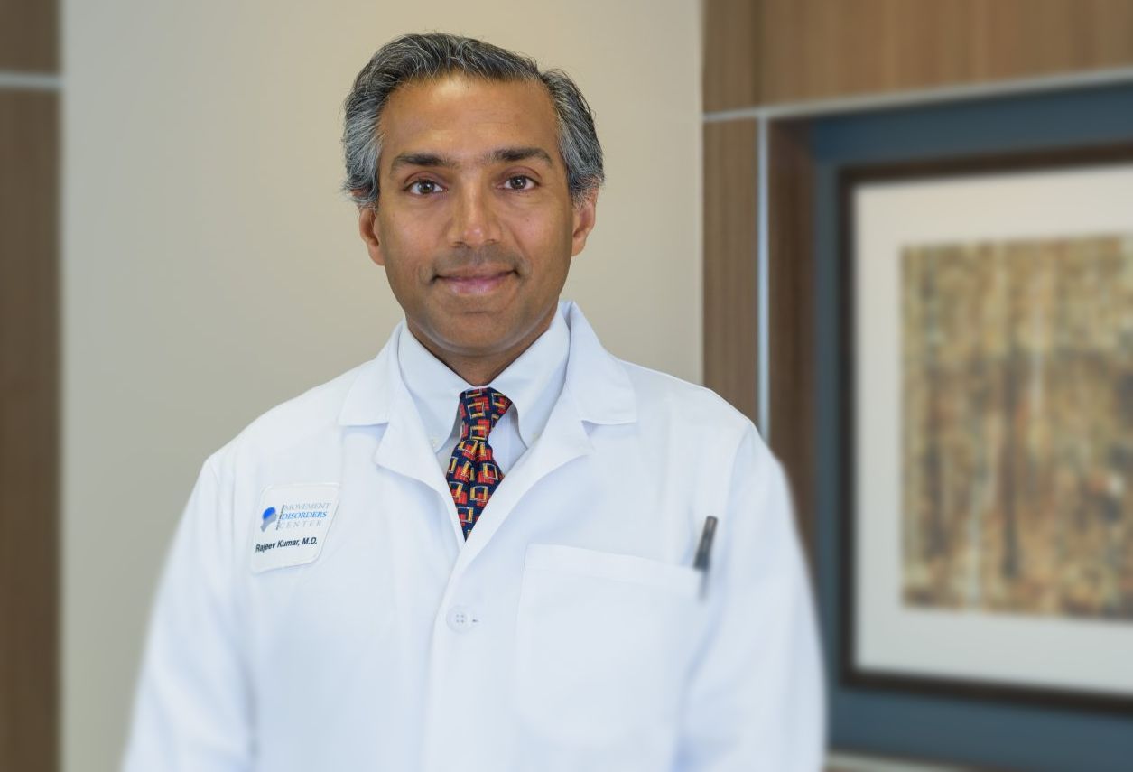 A doctor in a white coat and tie is standing in front of a picture.