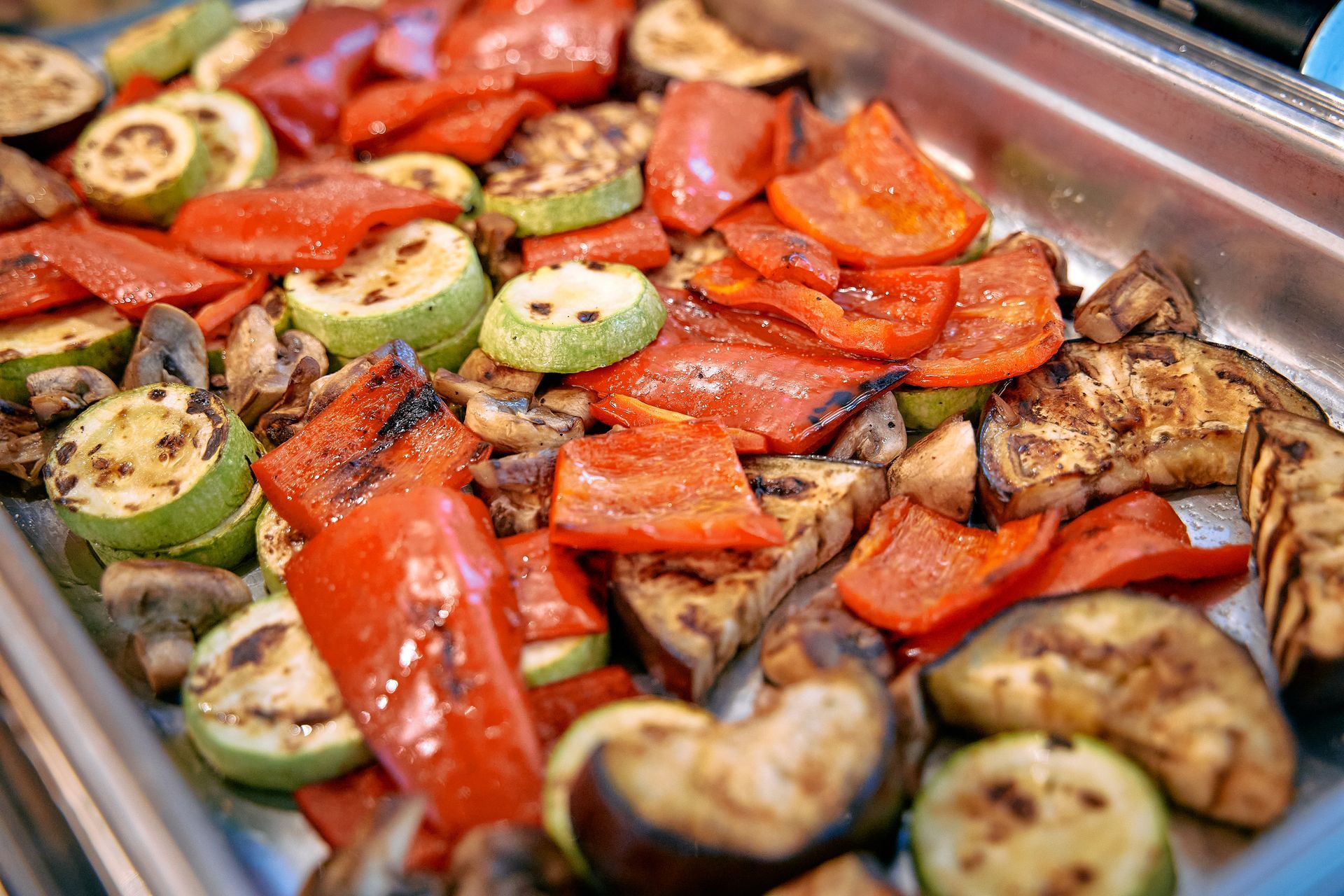 Grilled vegetables: red bell peppers, zucchini, eggplant, and mushrooms in a metal tray.