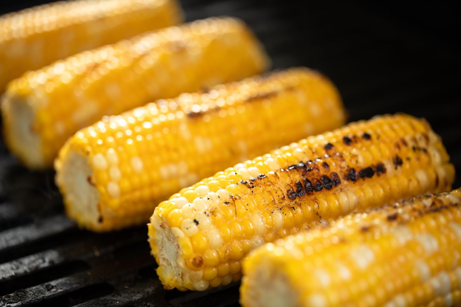 Grilled corn on the cob, yellow kernels, with char marks, on a black grill grate.