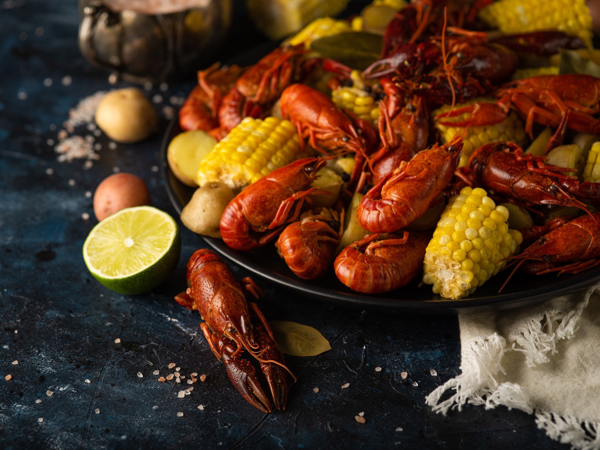 Crawfish boil with corn, potatoes, and lime on a dark plate.
