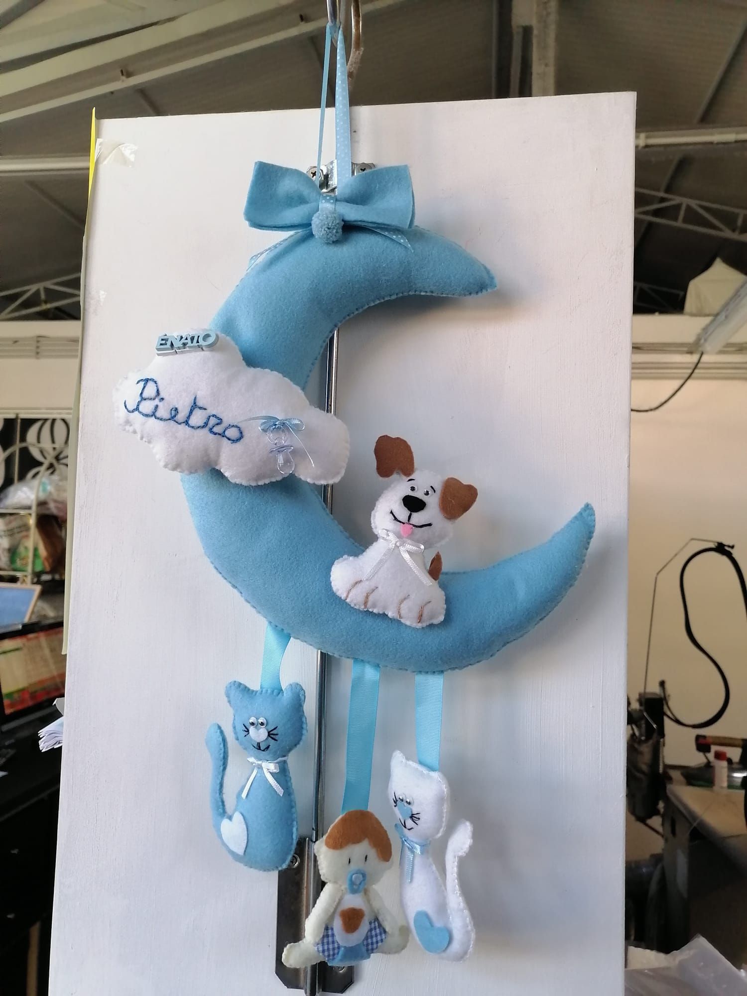 Una giostrina per la cameretta a forma di mezzaluna in feltro blu, con una nuvola su cui è scritto 