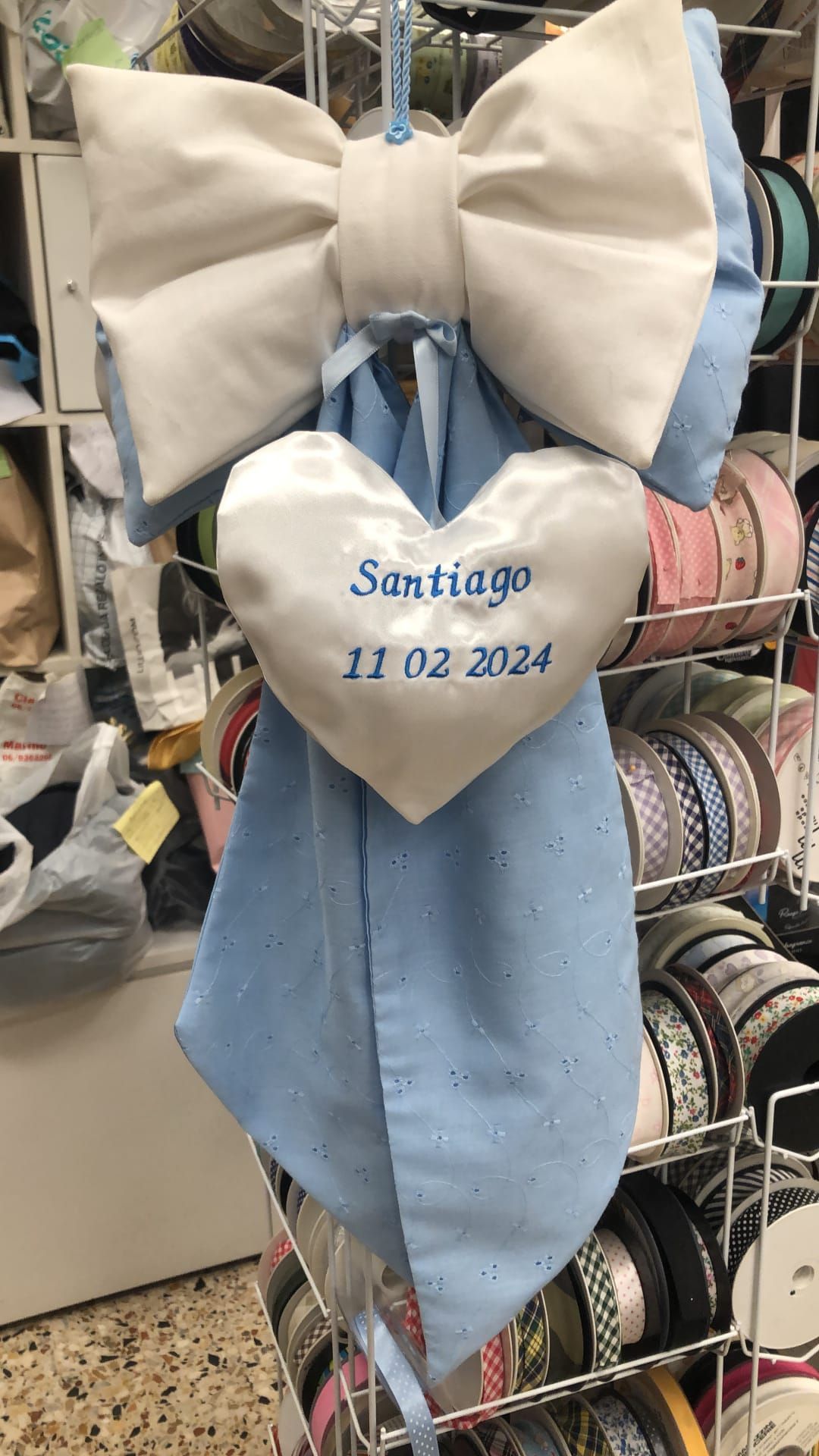 Un fiocco decorativo in tessuto blu e bianco con un'etichetta a forma di cuore ricamata con 