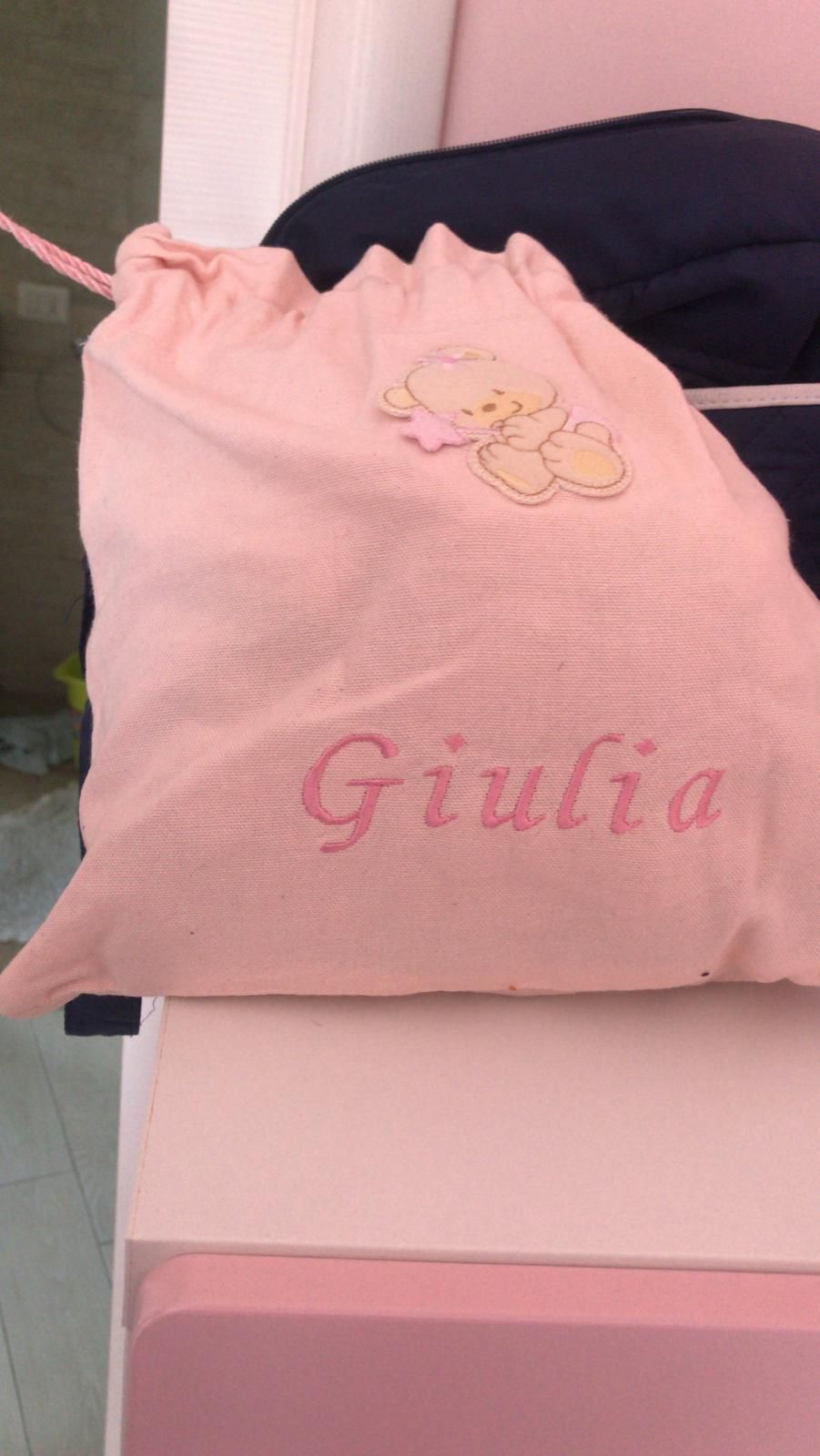 Una borsa di stoffa rosa con coulisse, ricamata con il nome 