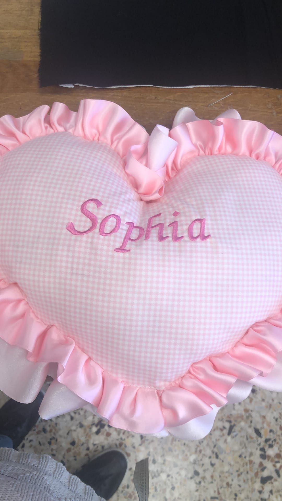 Un cuscino a forma di cuore in tessuto a quadretti rosa con bordo arricciato e il nome 