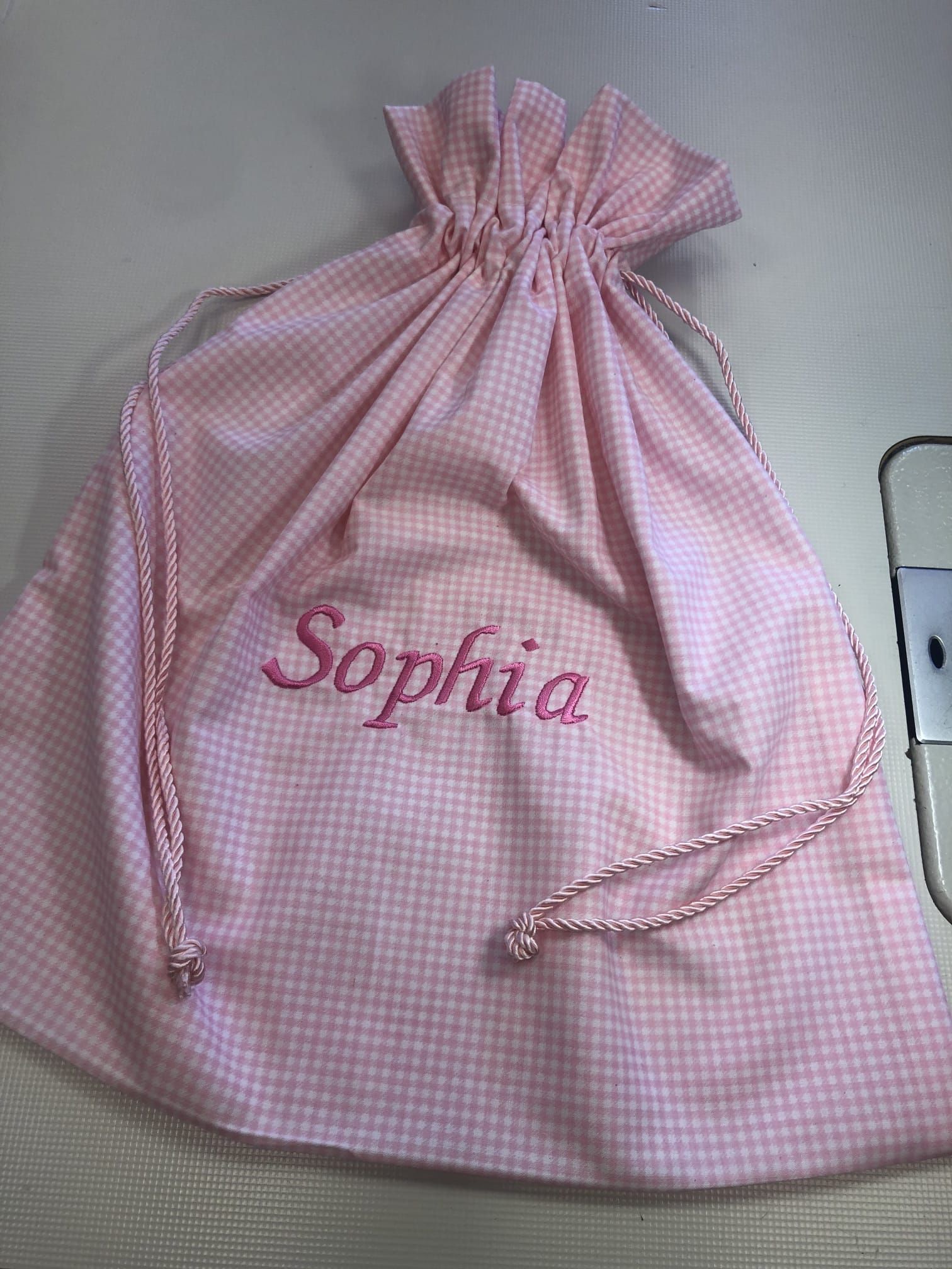 Una borsa in tessuto a quadretti rosa e bianchi con coulisse, su cui è ricamato il nome 
