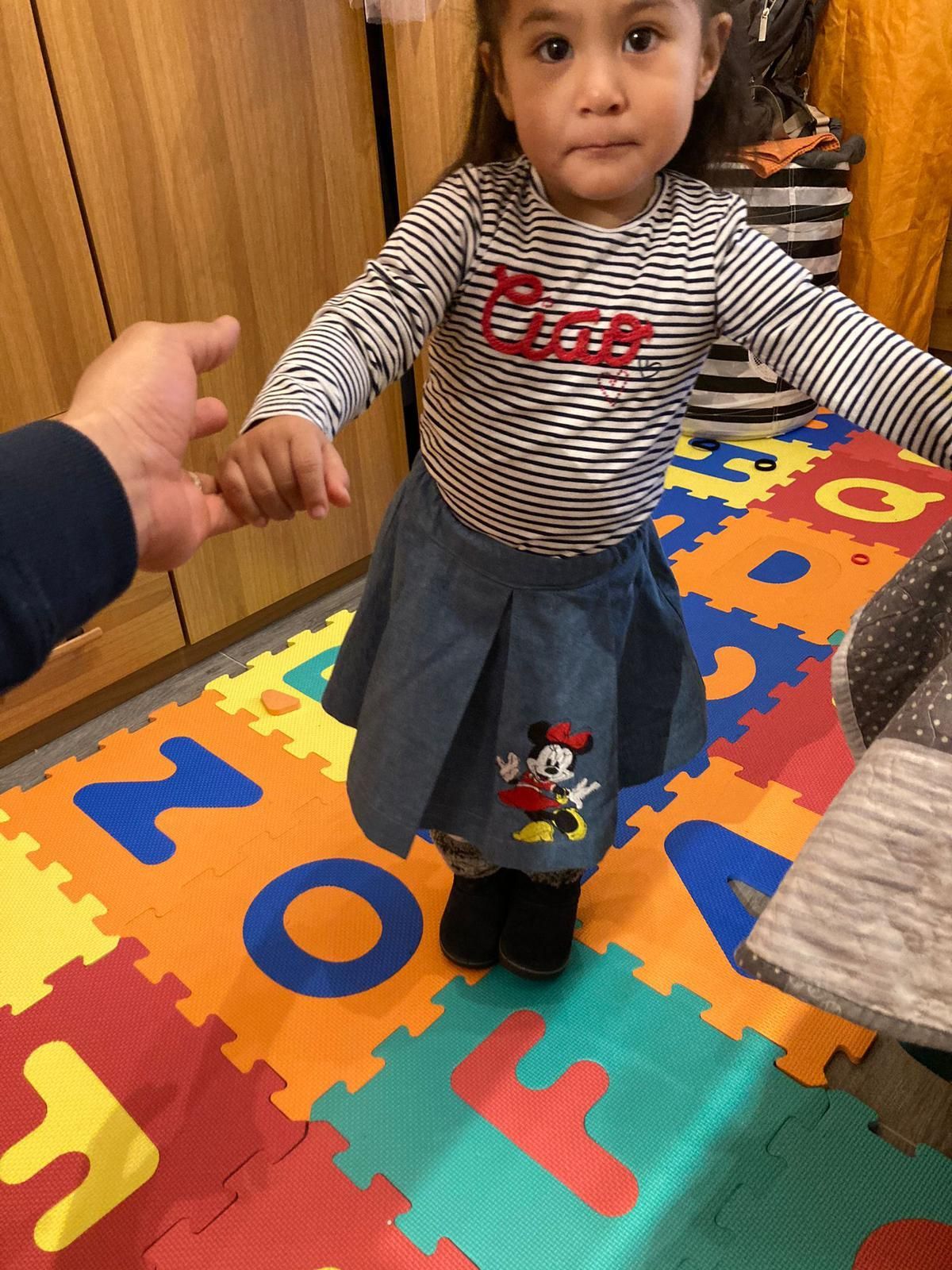 Una bambina tiene per mano un adulto mentre è in piedi su un tappeto da gioco in gommapiuma con l'alfabeto colorato