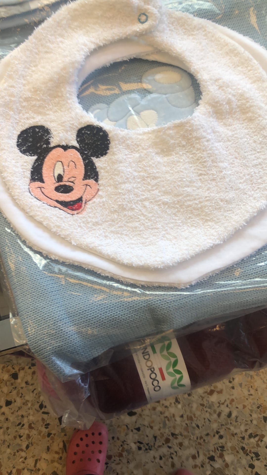 Un bavaglino bianco in spugna con l'immagine di Topolino, appoggiato su un involucro di tessuto blu.