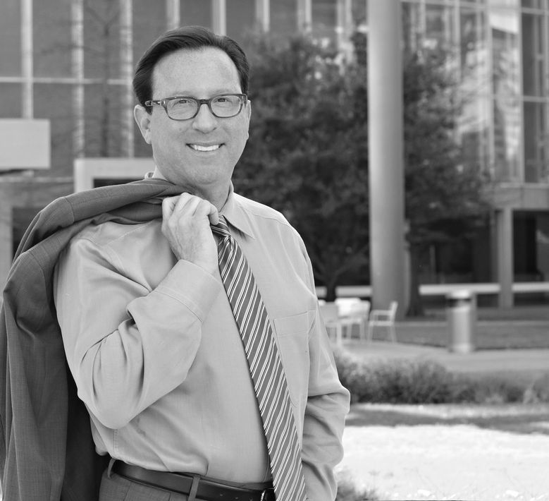 A man wearing glasses and a tie is carrying a jacket over his shoulder.