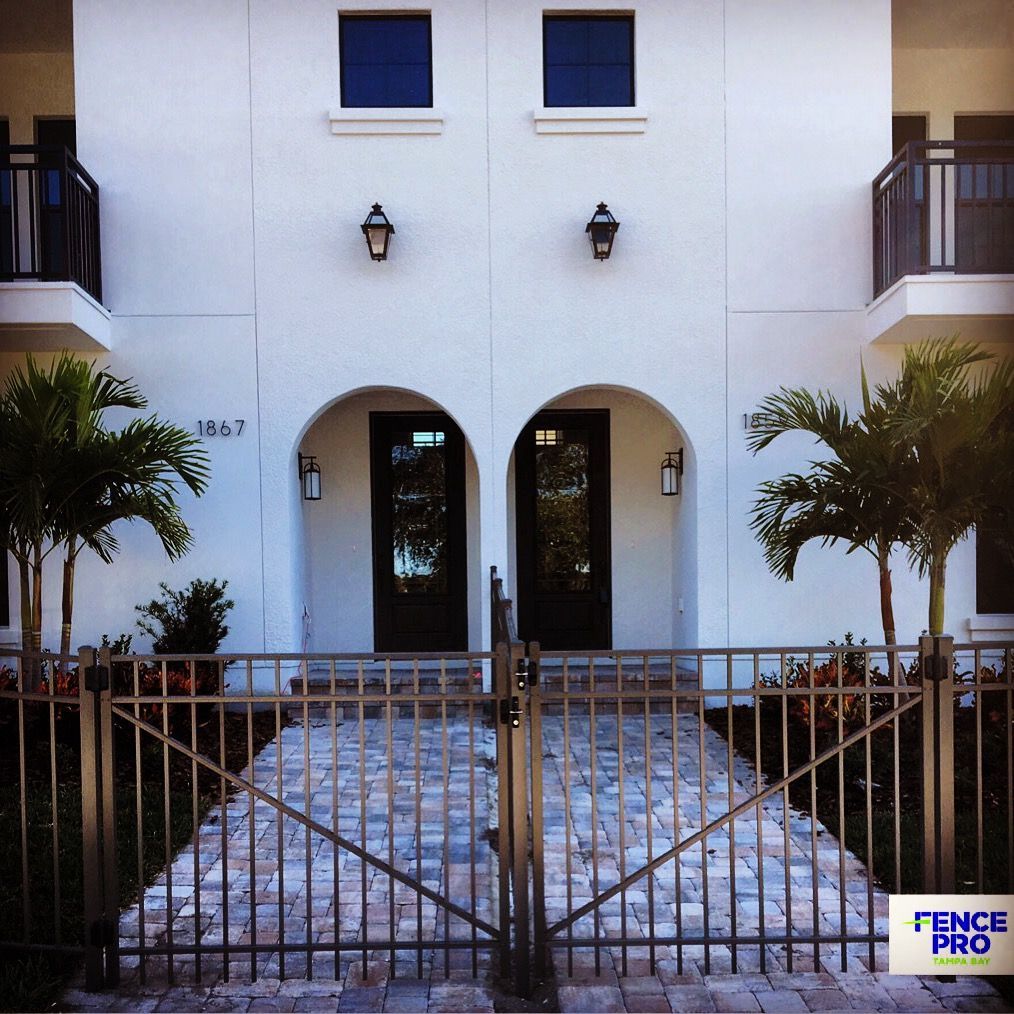 Front exterior of a white building with arched doors, windows, and an ornate metal gate leading to the entrance.