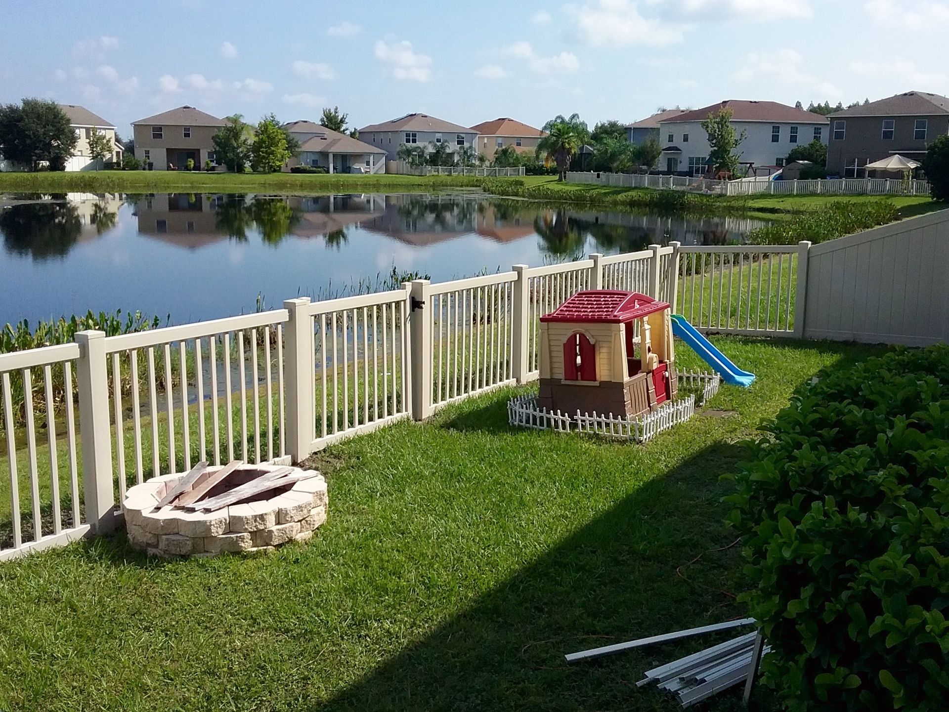 Backyard with a fence, lake, houses, a playhouse, fire pit, and fence.