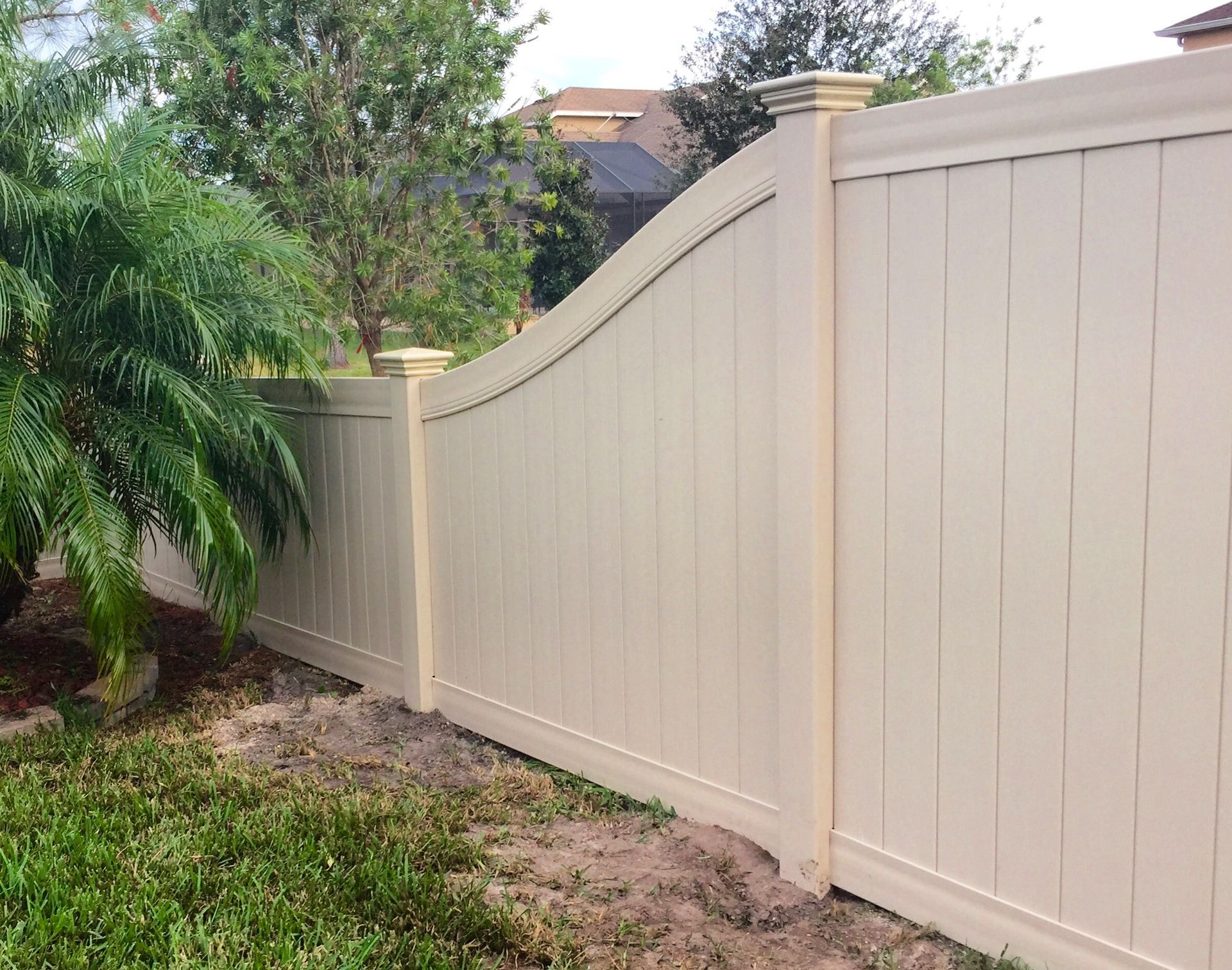 Tan vinyl fence in a backyard with landscaping.