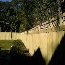 Wooden fence with lattice top, in sunny backyard, shadows cast.
